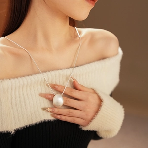 Détail d'un grand pendentif perle blanche ovale sur une fine chaîne argentée sur modèle