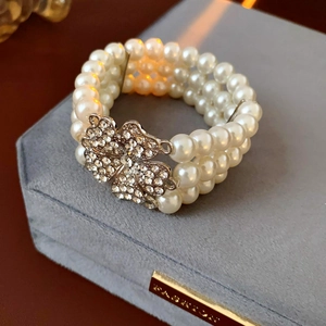 Close-up of triple-layer white pearl bracelet with rhinestone clover detail on velvet tray