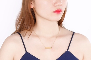 Close-up of golden bar pendant necklace with green crystal worn by a female model