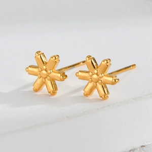 Macro detail of gold snowflake earrings with a matte finish on a white stone surface