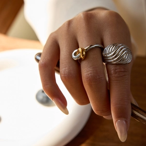 Close-up of stylish twisted gold and silver rings on hand showing metallic luster