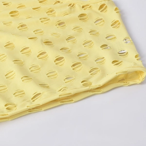 Macro view of light yellow knitted fabric with horizontal distressed hollow cutouts