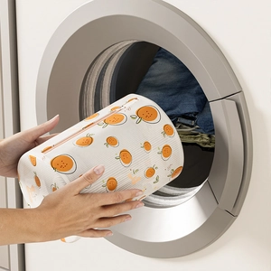 Fine mesh laundry bag with orange print being placed into a washing machine
