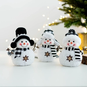 Three plush Christmas snowman figures with black and white plaid scarves near a lit tree