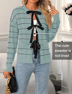 Detail of light blue cable knit cardigan with three black ribbon bow closures