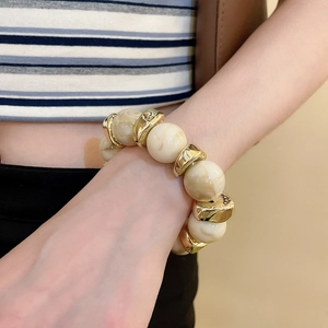 Close-up of marble-textured acrylic beads and gold geometric spacers on a beaded bracelet