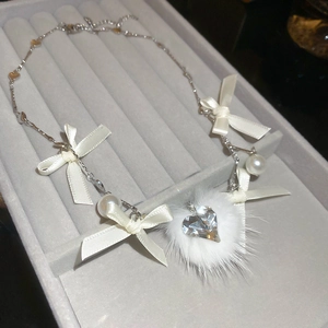Detail of satin ribbon bows, faux fur pompom and heart-shaped rhinestone on pearl necklace