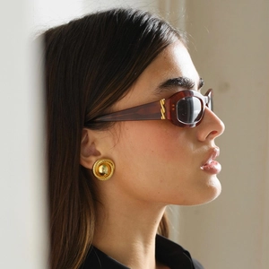 Close-up of vintage golden spiral textured stud earrings and oval sunglasses on a model