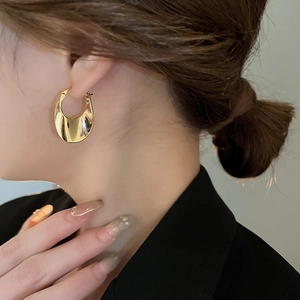 Close-up of elegant wide gold geometric hoop earrings worn with a formal black suit