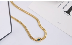 Macro detail of golden Evil Eye pendant with blue stone on flat woven link chain necklace