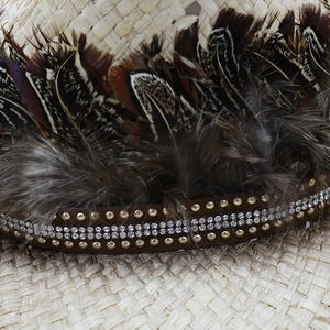 Detail of raffia cowboy hat featuring ethnic feathers, brown suede band, and sparkling rhinestones
