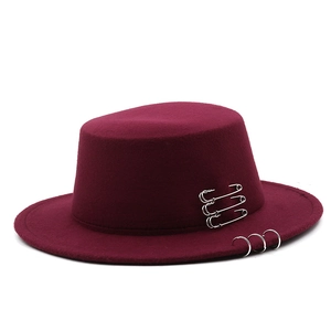 Close-up of burgundy flat top wool hat with silver safety pins and metal ring details