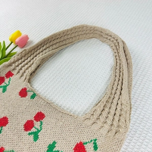 Detailed texture of knitted tote bag featuring red and green cherry patterns on beige yarn