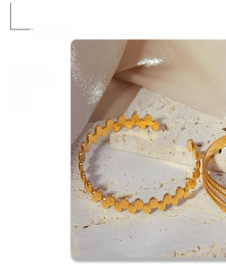 Detail of 18K gold-plated titanium geometric wavy cuff bracelet on a white stone base