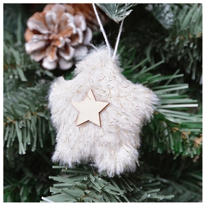 Detail of plush beige star ornament with wooden center hanging on a Christmas tree