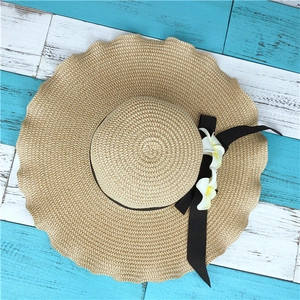 Detail of wide brim straw hat with decorative frangipani flowers and black ribbon bow