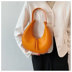Close-up of bright orange crescent leather bag with double zippers worn with white blazer