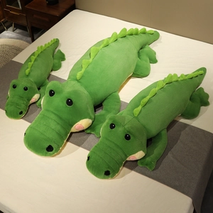 Peluches crocodiles verts en trois tailles présentées sur un lit blanc confortable