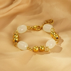Detail of gold beaded bracelet with white resin stones on champagne silk fabric background