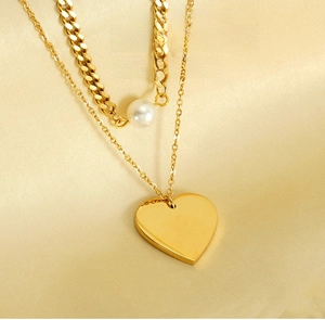 Detail of double-layer gold necklace with heart pendant and pearl on silk fabric