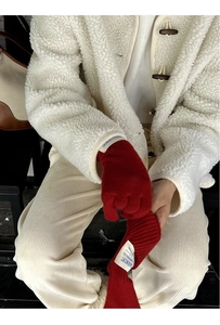 Detailed close-up of red knit wool gloves with garment tag on a white fleece sleeve