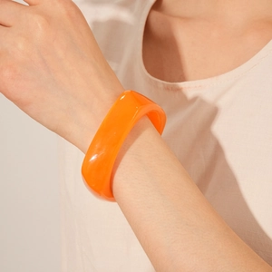 Close-up of a thick orange resin bangle showing its smooth texture and stylish marble effect