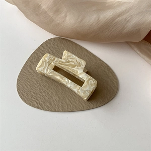 Detail of beige marble texture acetate hair claw clip on soft cream silk and leather