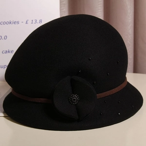 Dettaglio di un cappello cloche in lana nera vintage con fiore in feltro e perle