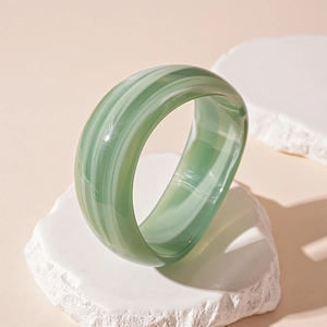 Macro view of green and white marbled acrylic wide cuff bracelet on stone stand