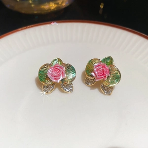 Detailed macro view of pink rose floral earrings with green leaves on ceramic plate