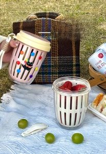 Outdoor picnic scene showing a portable fruit cup with built-in strainer and cute cat prints
