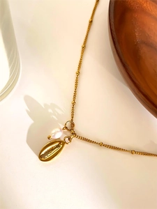 Detailed shot of golden sea shell pendant with freshwater pearl on a thin chain
