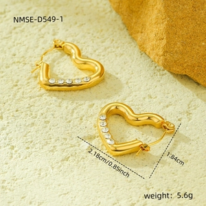 Macro detail of gold heart earrings with zircons and product dimensions on sand background