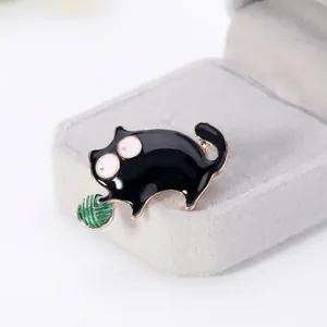 Detailed view of a black enamel cat brooch hugging a green yarn ball with gold edges