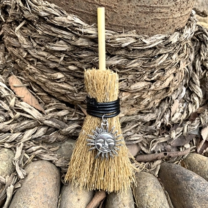 Macro detail of wicca mini broom with silver sun pendant on natural rustic background