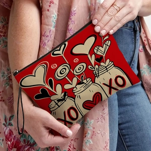 Red heart print makeup bag with black zipper and wristlet strap held by a model