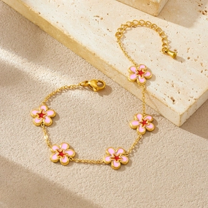 Close-up of gold chain bracelet with five pink flower charms on a textured stone base