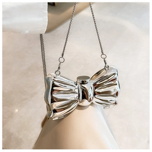 Detail of a shiny silver bow-shaped mini acrylic bag with a thin metal chain strap