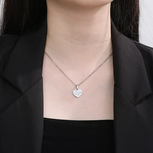 Close-up of a silver heart pendant necklace with Love engraving worn by a model