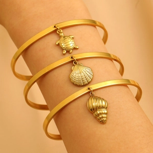 Gold stainless steel bangles featuring sea turtle, seashell, and conch charms on a wrist