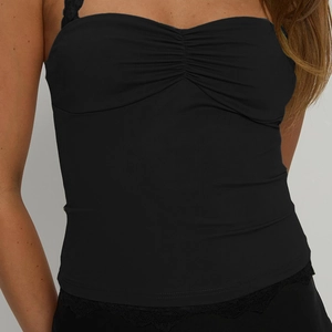 Close-up of black backless halter top featuring pleated bust and delicate lace hem detail