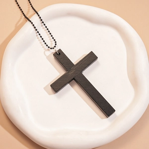Détail d'un pendentif croix en bois noir avec chaîne perlée sur un plateau blanc