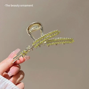 Detail of gold metal flower hair claw clip with green rhinestones and tassel design