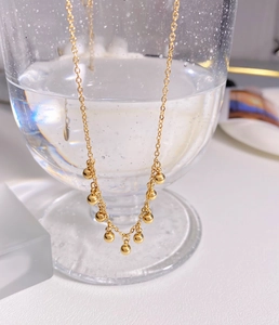 Close-up of gold beaded fringe necklace hanging on a clear glass edge with water