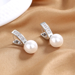 Close-up of pearl drop earrings with baguette-cut zircon inlay on silver hoops