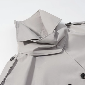 Detailed close-up of light gray trench coat with high collar and epaulette buttons