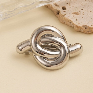 Close-up of a silver polished metal knot hair tie against a minimalist stone background