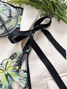 Detail of green butterfly embroidery on sheer mesh with elegant black satin ribbon bow
