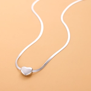 Detail shot of a minimalist silver heart pendant on a sleek snake chain necklace