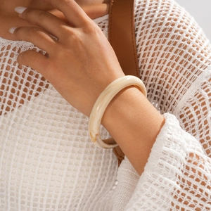 Detail of chunky cream marble resin bangle worn on wrist with white knit texture